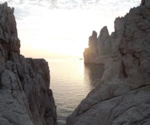 Solnedgangsudsigt over et roligt hav indrammet af forrevne kalkstensklipper, der skaber en smal passage. Himlen har en blød gradient af farver, og klippeformationerne tilføjer dramatisk kontrast til det fredfyldte vand.